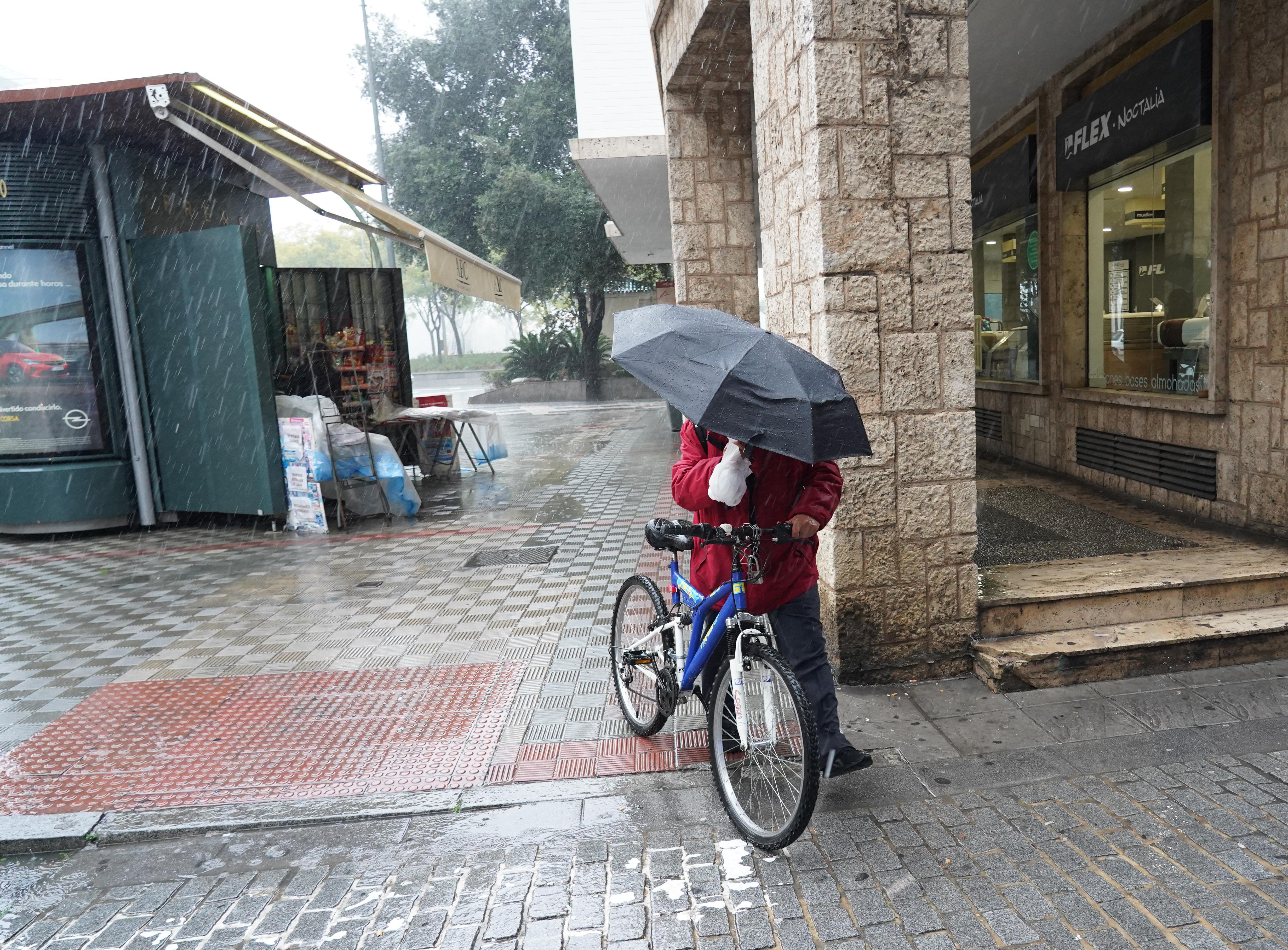 Un ciclista con un paraguas resguardándose de la lluvia
