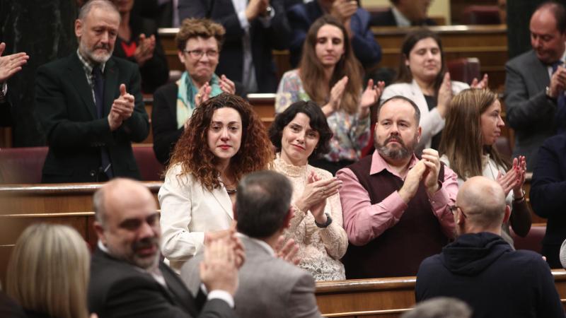 La diputada de Unidas Podemos Aina Vidal (con chaqueta blanca) se emociona al recibir el aplauso de su bancada junto a la socialista tras el agradecimiento que le ha expresado Pablo Iglesias por