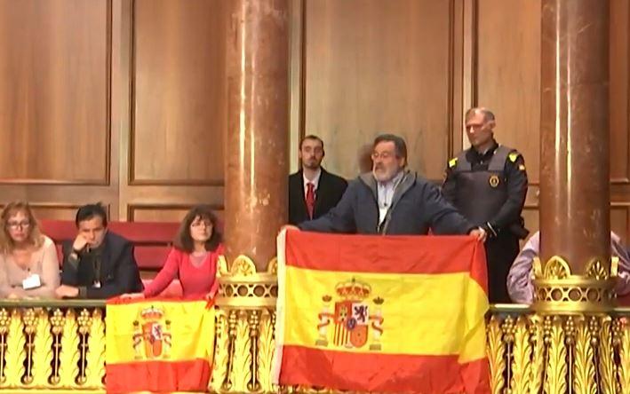 Un hombre muestra una bandera de España en el pleno del Ayuntamiento de Barcelona