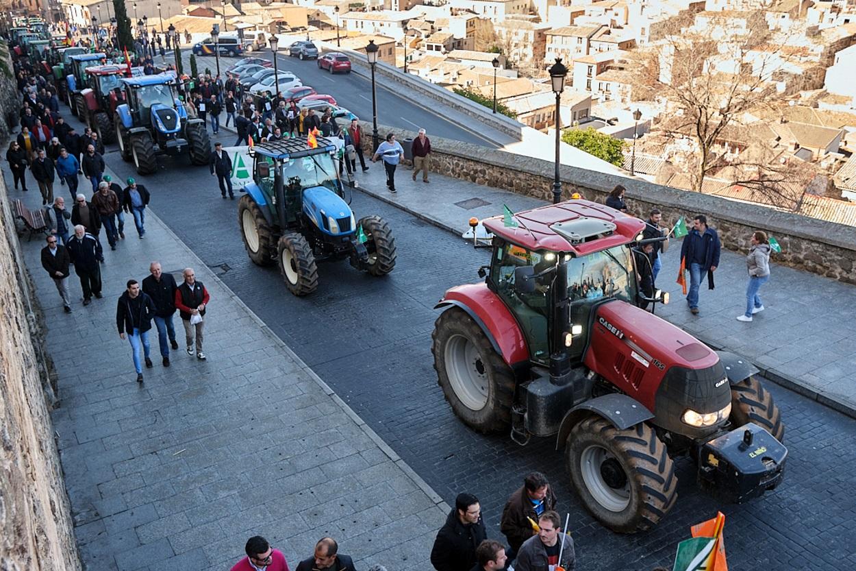 Una fila de tractores avanza por las calles de Toledo, junto a los asistentes a la manifestación de agricultores y ganaderos en Toledo Castilla La Mancha (España)