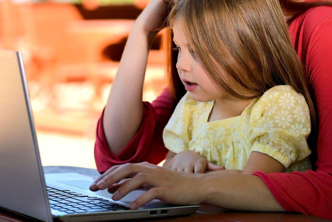 Una niña utilizando un ordenador con uno de sus progenitores