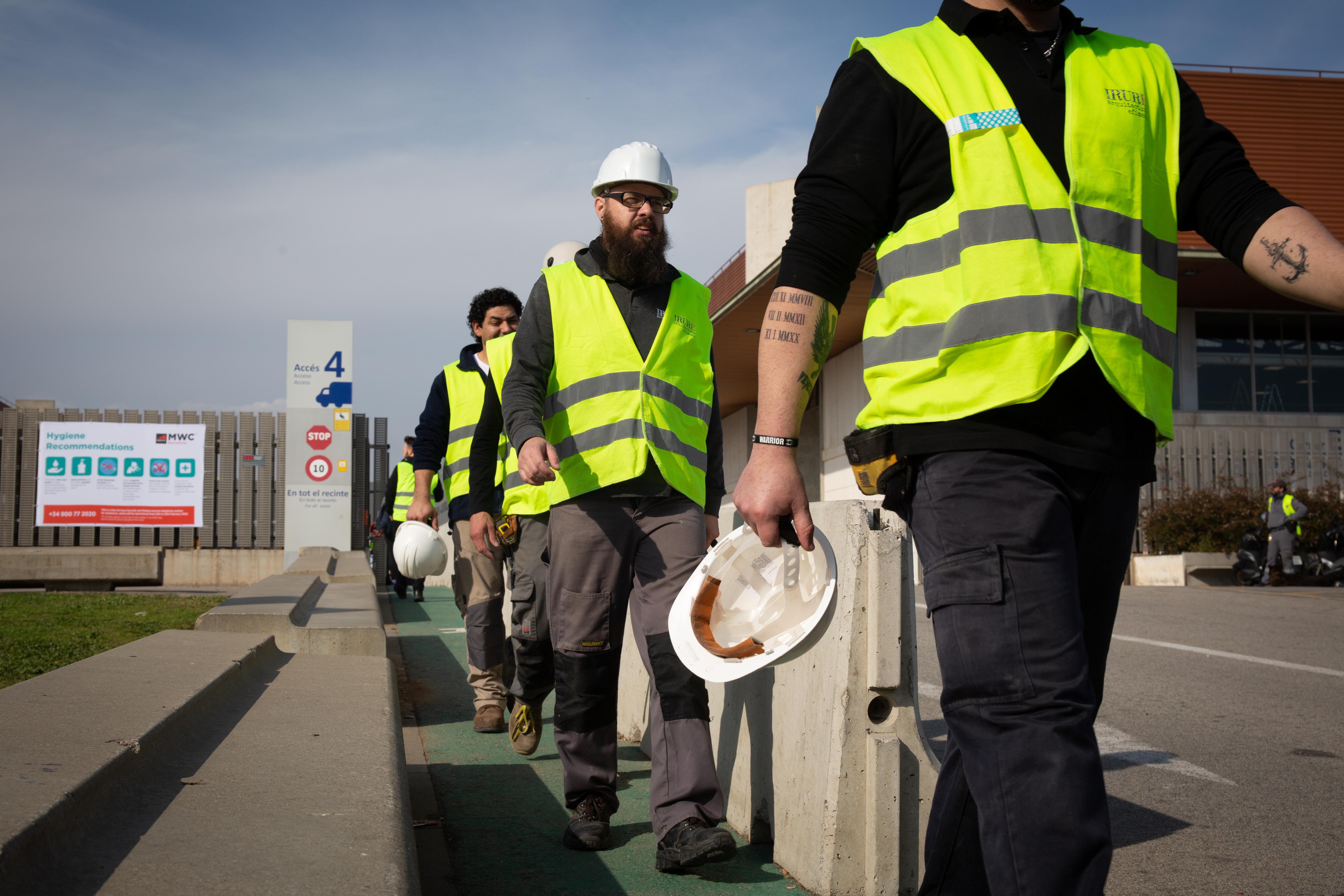 Varios trabajadores con chalecos amarillos y cascos blanco en el acceso 4 del recinto del Mobile World Congress (MWC) durante el desmantelamiento de los stands de la feria tras su can