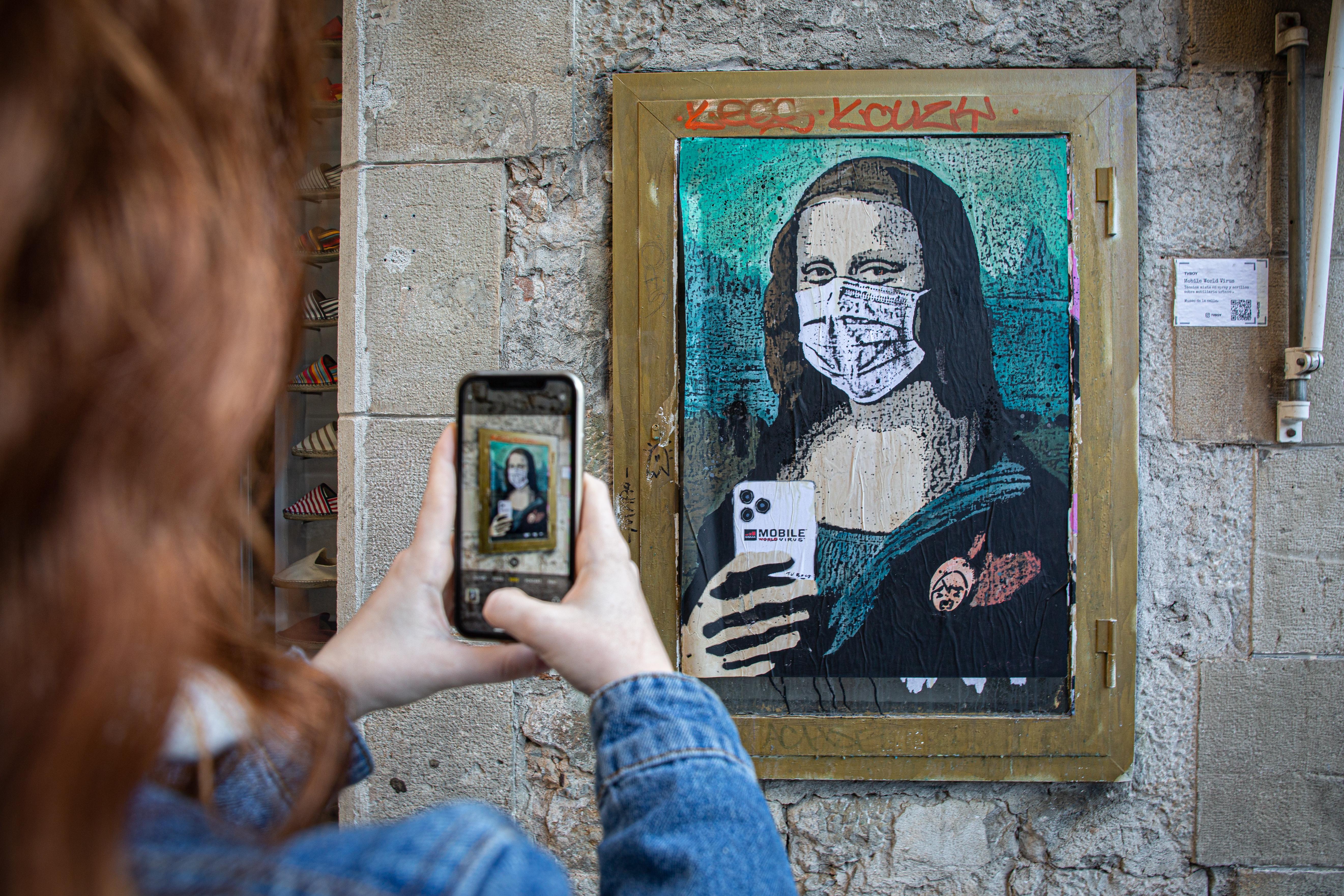 EuropaPress 2660102 Una mujer hace una foto a una pintura de una Gioconda con un móvil y una mascarilla obra del grafitero TV Boy llamada 'Mobile World Virus' en referencia a la cancelación del Mobile Wo