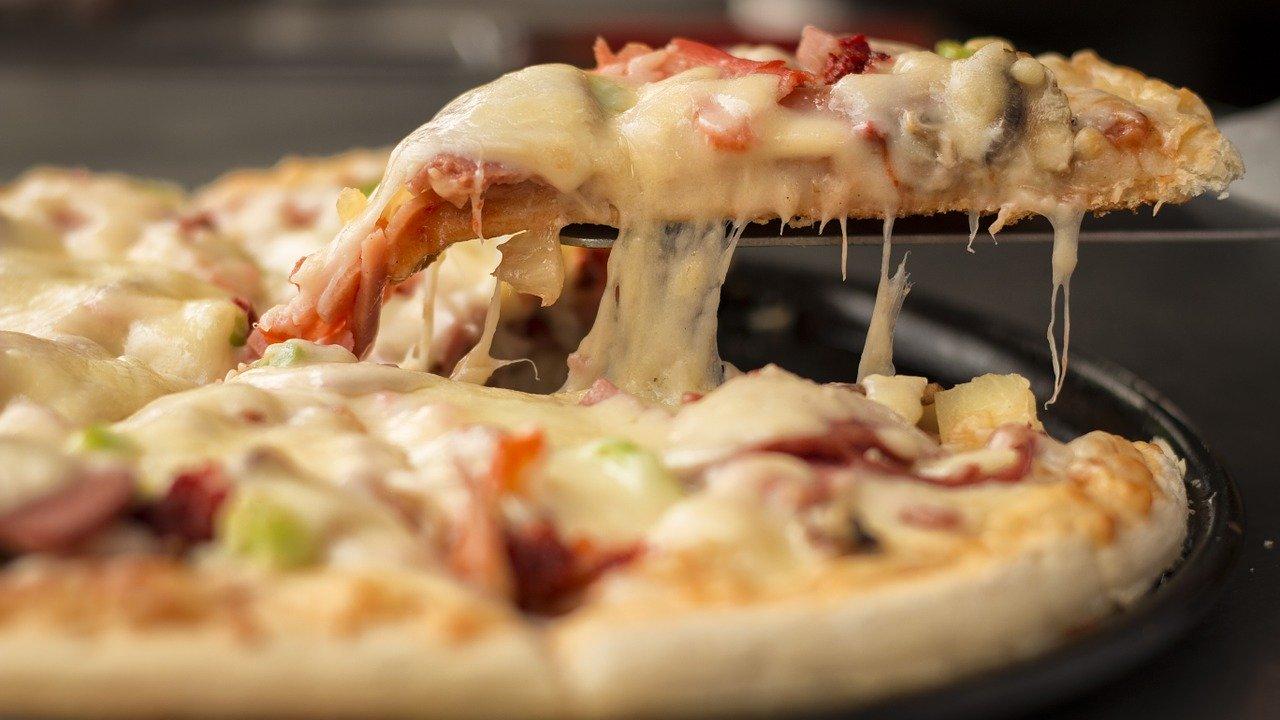 Una persona corta un trozo de pizza. Fuente: Pixabay.