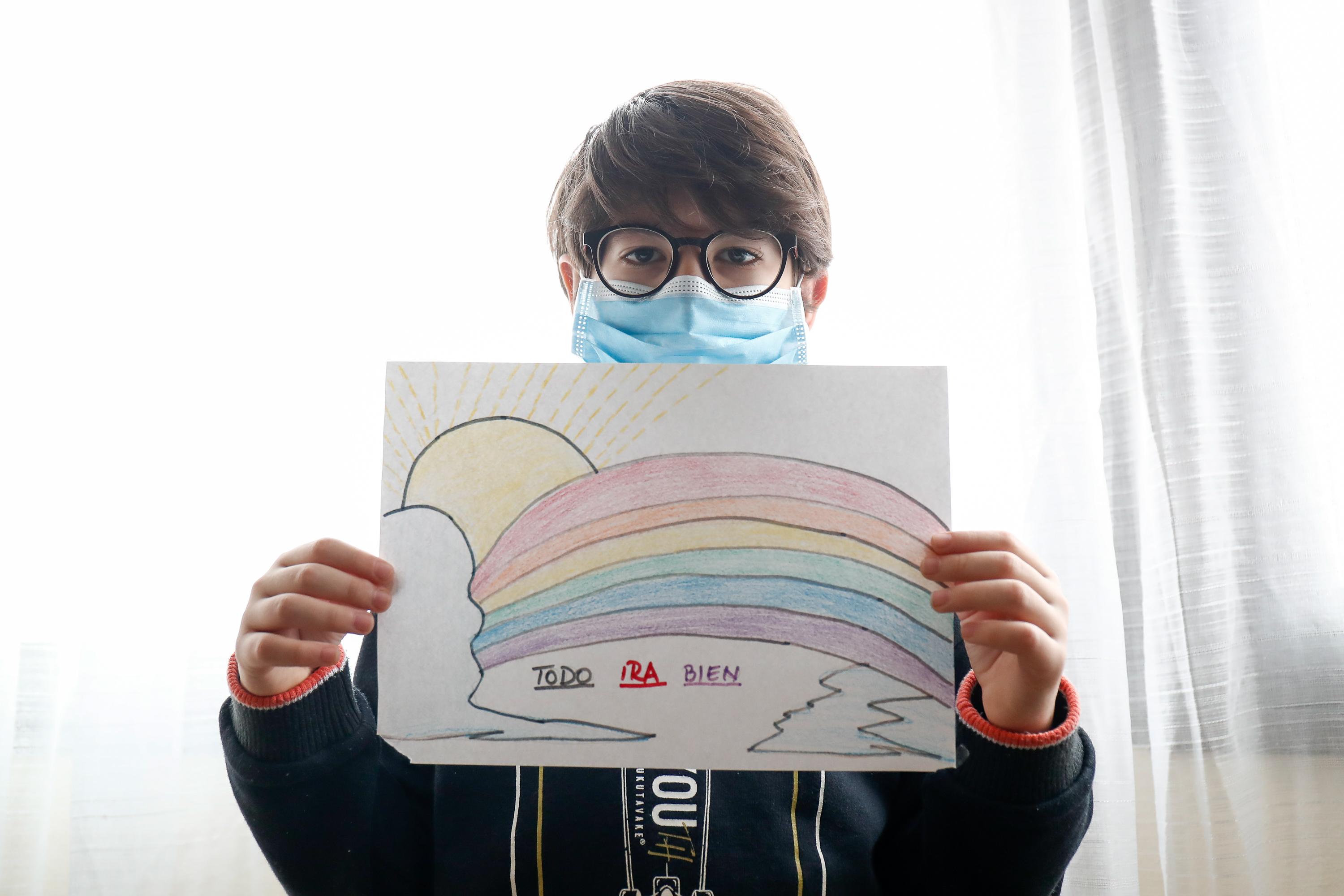 Un niño con mascarilla enseña un dibujo que ha hecho de un arcoiris y la frase 'Todo irá bien' 