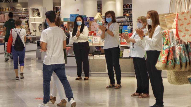 Varias dependientas de un comercio protegidas con mascarilla aplauden respetando la distancia de seguridad en el primer día de la Fase 2 de desescalada