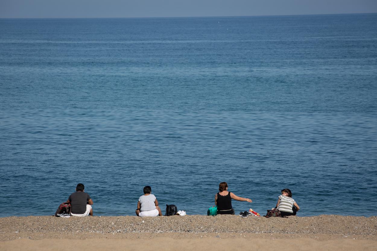 Varias personas sentadas en la Playa de la Barceloneta