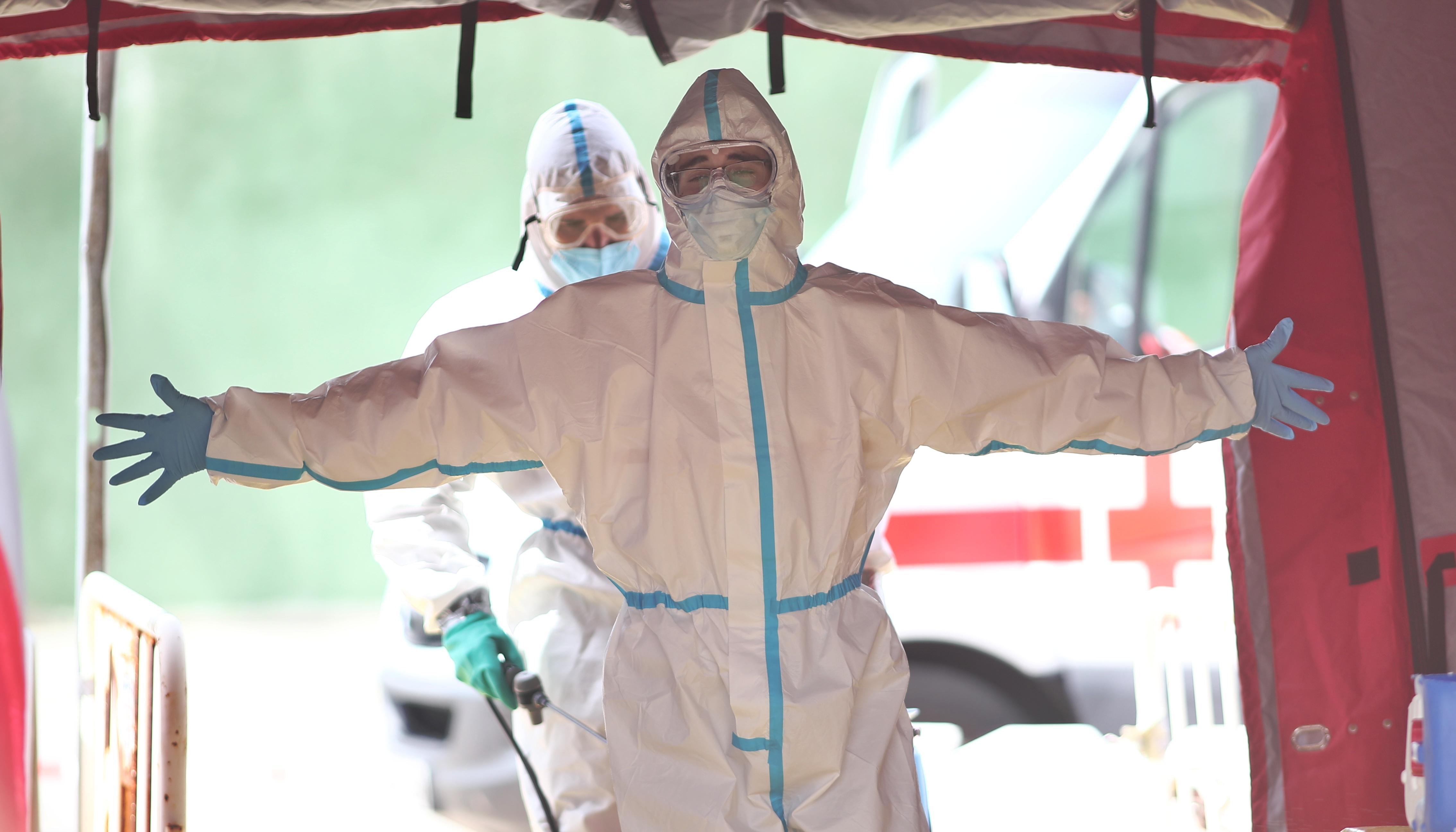 Un Bombero de la Comunidad de Madrid protegido con un traje blanco desinfecta a un sanitario de una ambulancia de la Cruz Roja Española en el Parque de Bomberos de Coslada. EP