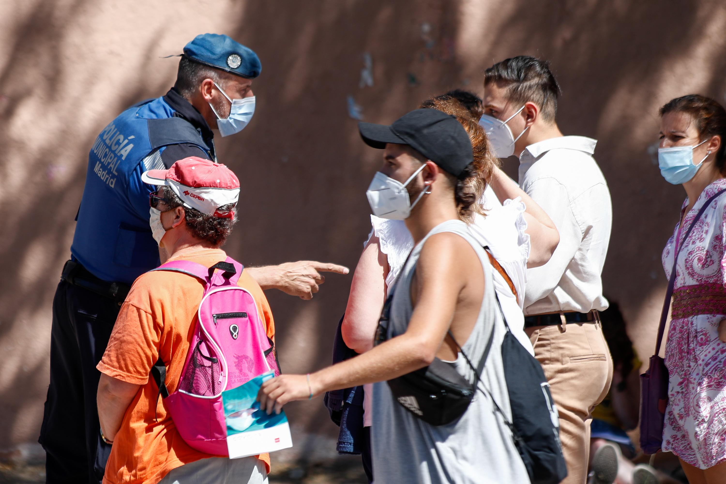 Un agente de la Policía Municipal de Madrid habla con una de las personas que guardan cola en el IES Virgen de la Paloma para realizarse test de coronavirus, en Madrid (España),