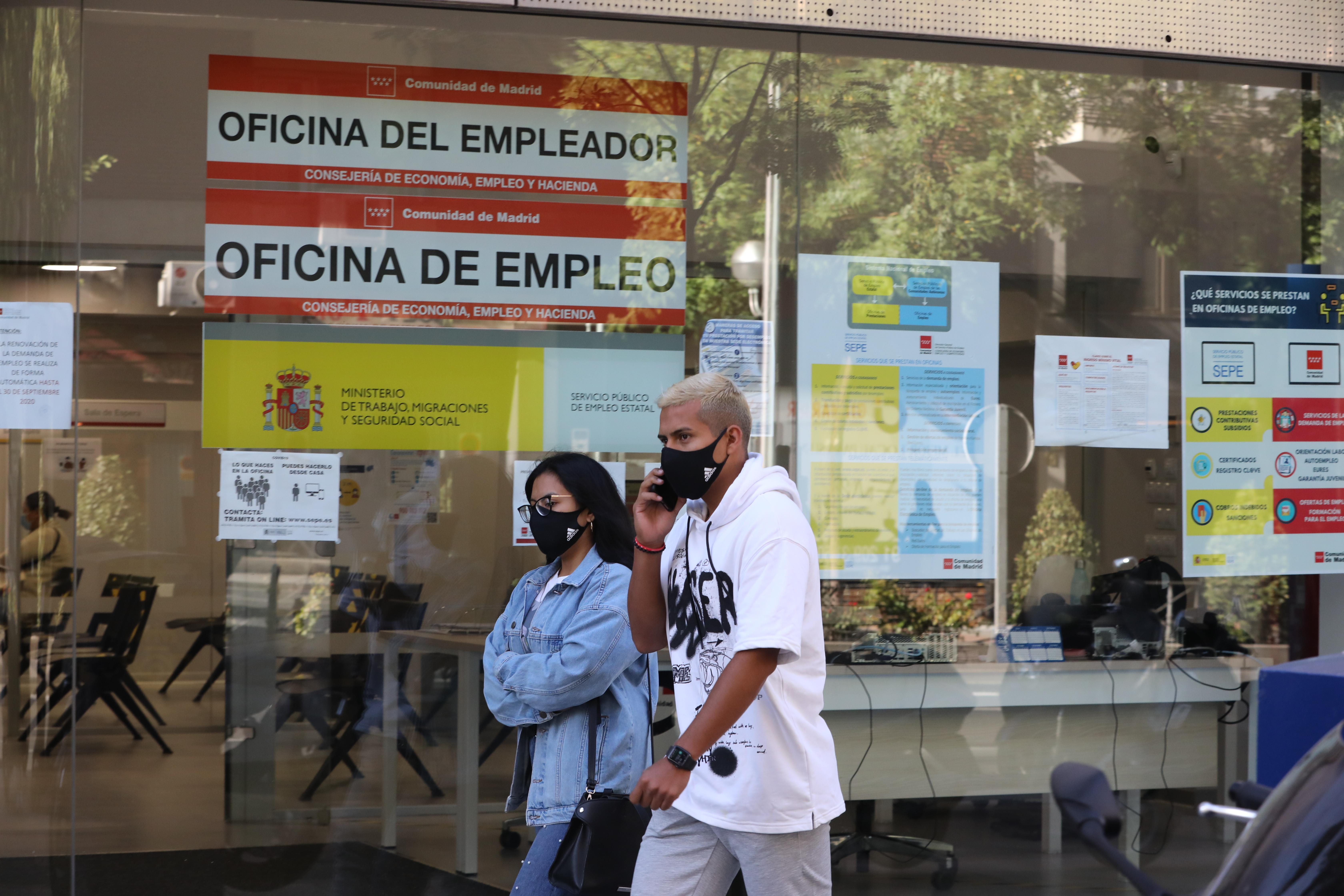 Una pareja con mascarilla pasa por una oficina de empleo de Madrid (España).