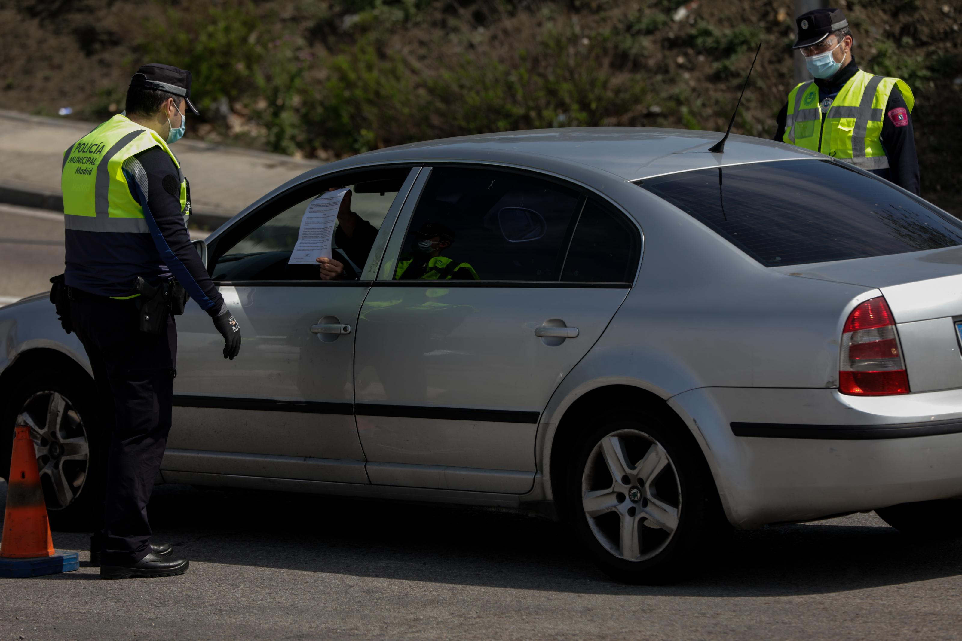 Un conductor muestra a un agente de la Policía Municipal protegido con mascarilla el justificante que le permite salir de casa en un control policial de tráfico en el barrio madrileño de Vallecas / EP