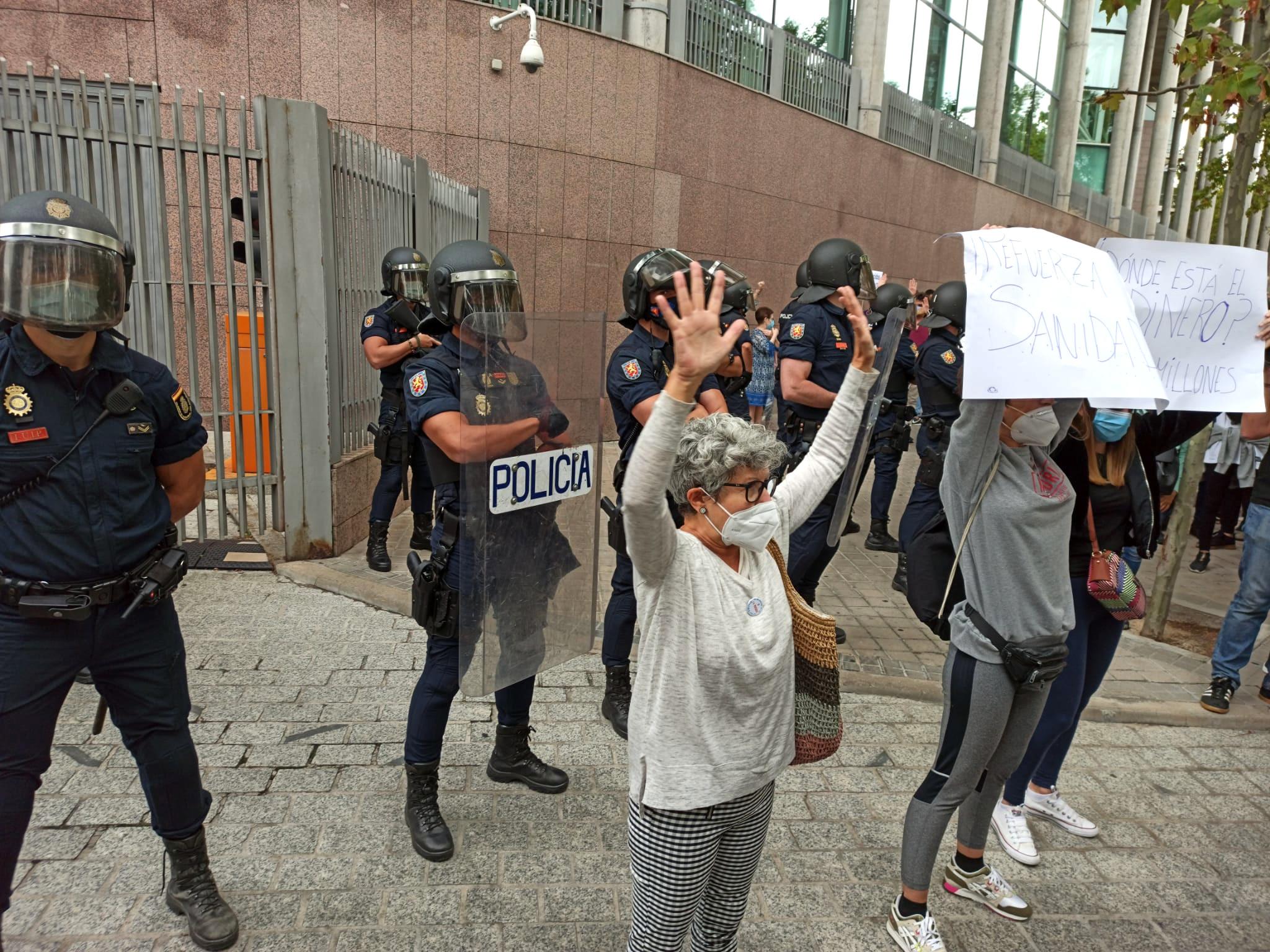 Participantes en una de las concentraciones convocadas durante la jornada de hoy contra los confinamientos selectivos en determinados distritos levantan las manos frente a la Asamblea como signo de protesta