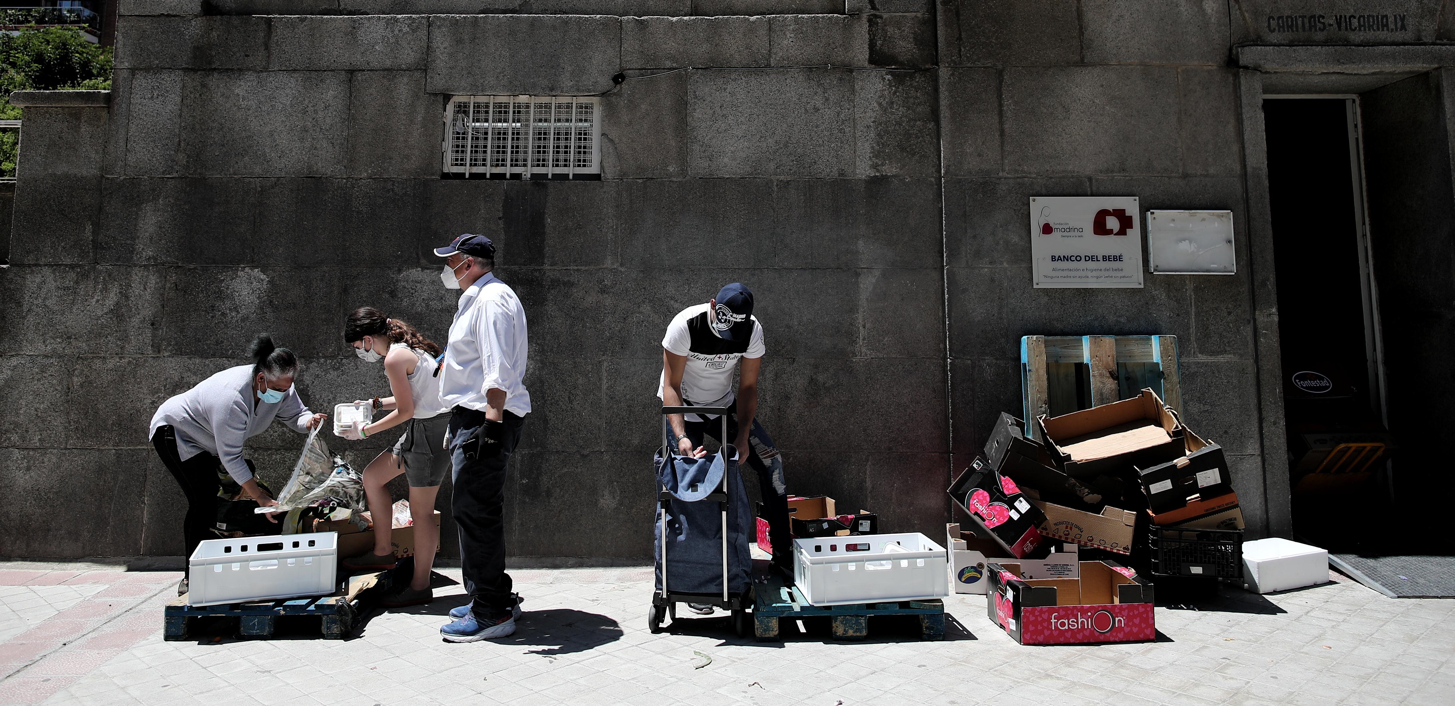 Dos personas recogen alimentos que les dan dos voluntarios a las puertas de la Parroquia Santa María Micaela, en Madrid. Fuente: EP.