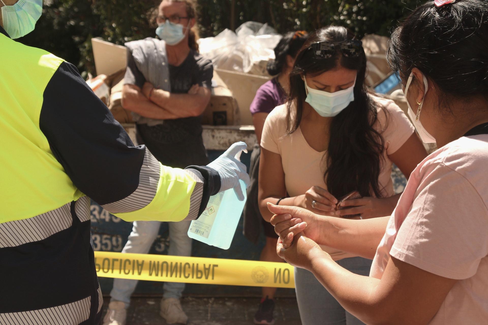 Un sanitario proporciona gel hidroalcohólico a varias personas que esperan en el dispositivo para realizar PCR aleatorias en Vallecas