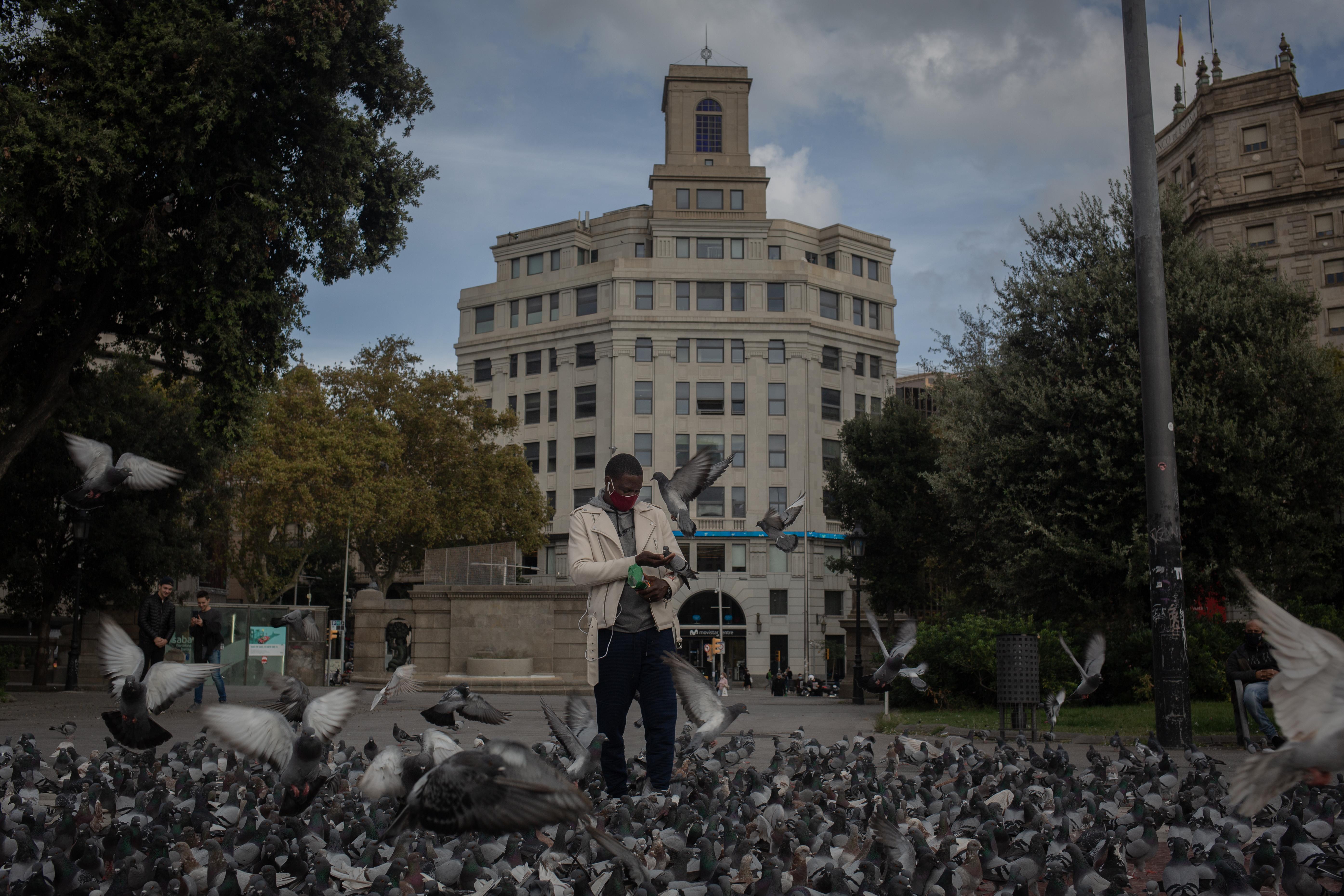 Un hombre da de comer a las palomas durante el tercer día de la entrada en vigor de las nuevas restricciones en Cataluña, en Barcelona,