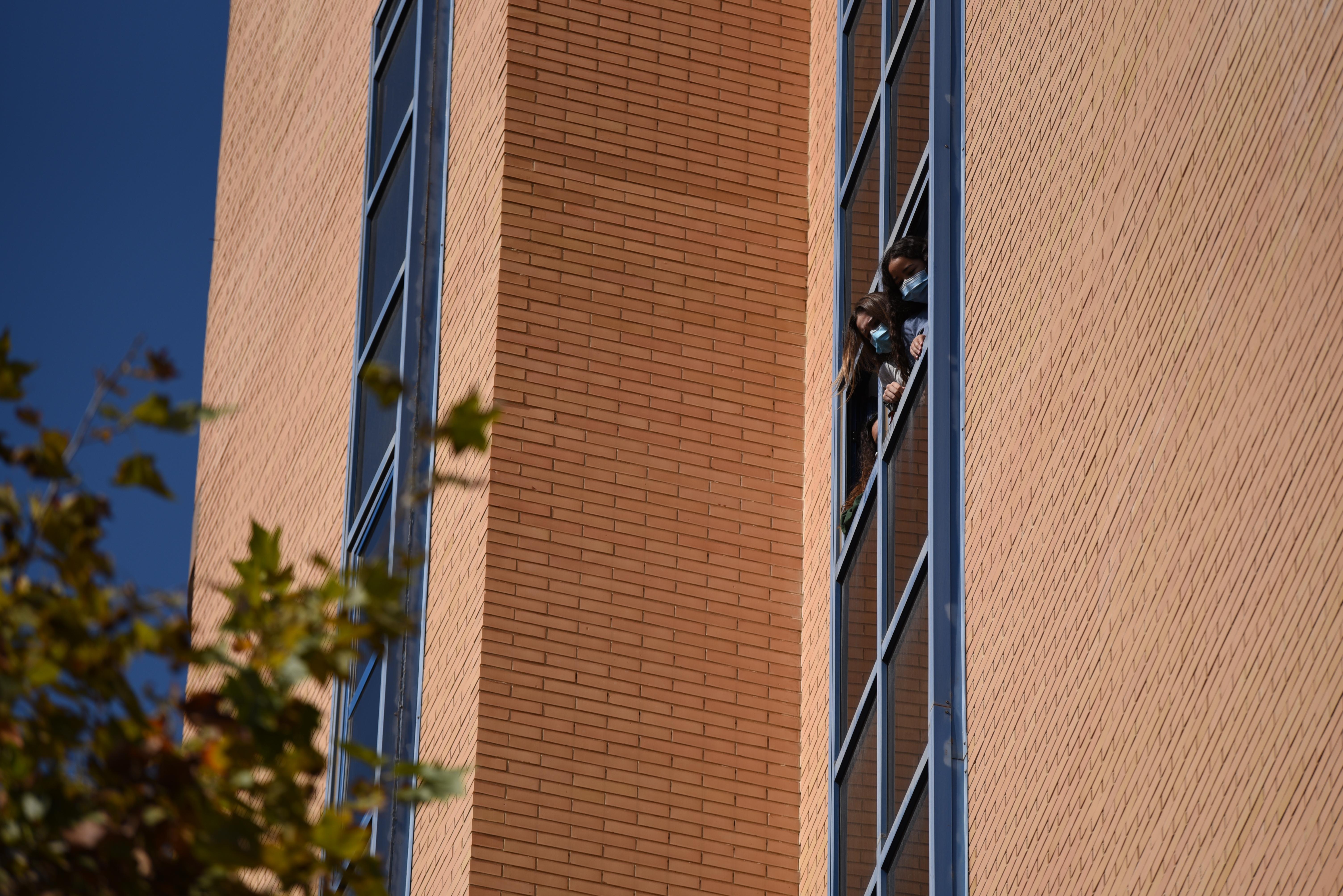 Dos estudiantes se asoman a una ventana de la residencia Galileo Galilei durante una concentración convocada por el sindicato 'Estudiantes en Lucha' en la residencia Galileo Galilei.