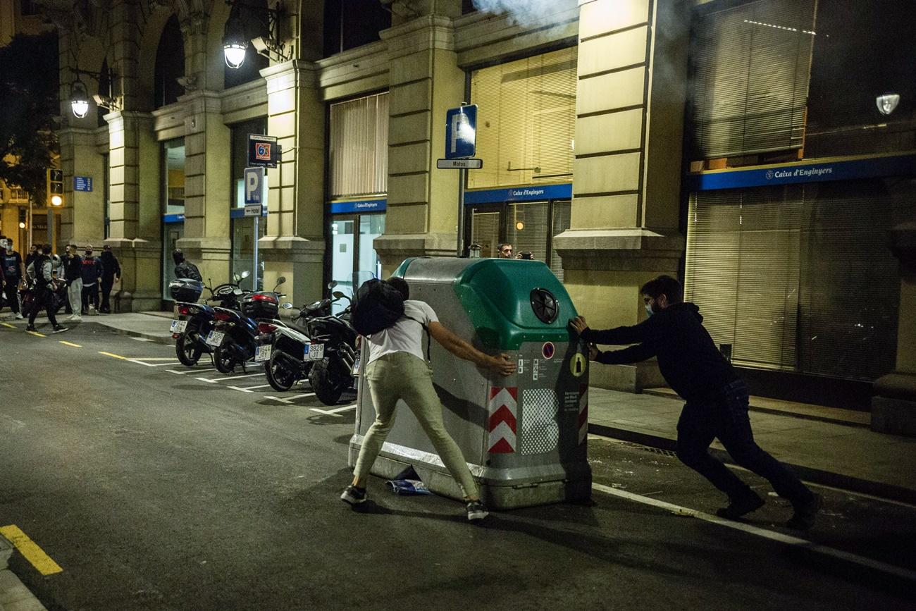 Dos jóvenes arrastran un contenedor en las protestas de Barcelona contra las restricciones para frenar la pandemia